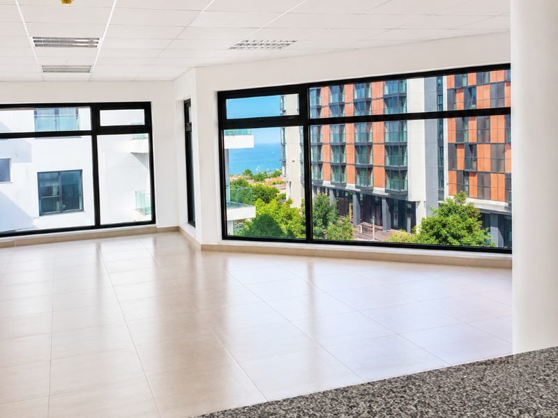 A bright, vacant office space featuring large windows with urban views, a suspended ceiling with recessed lighting, and a granite-topped service counter.