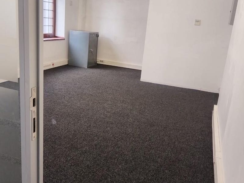 An empty office space featuring dark carpeting, exposed HVAC ducting, and a leaded glass window, providing a functional blank canvas for professional use.