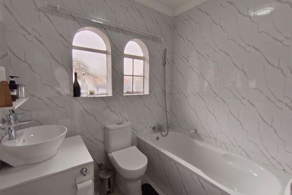A modern bathroom featuring marble-effect wall tiles, a vessel sink vanity, a toilet, and a bathtub with a shower mixer.