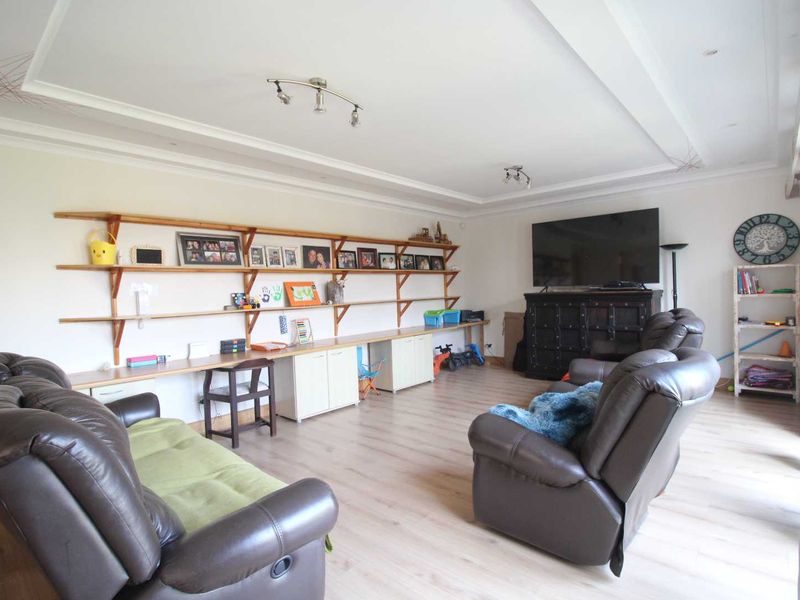Spacious living room featuring light laminate flooring, recessed ceiling detail, and extensive built-in shelving and desk cabinetry along the wall.