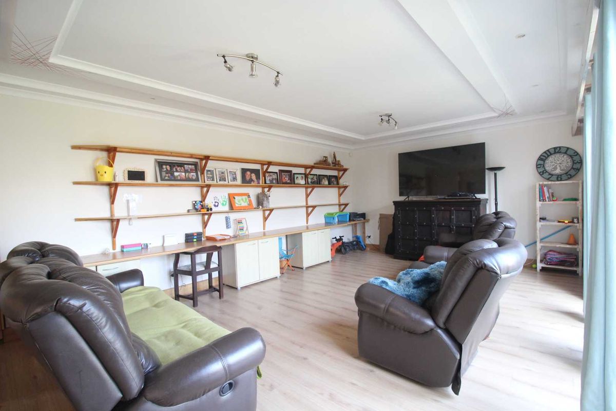 Spacious living room featuring light laminate flooring, recessed ceiling detail, and extensive built-in shelving and desk cabinetry along the wall.