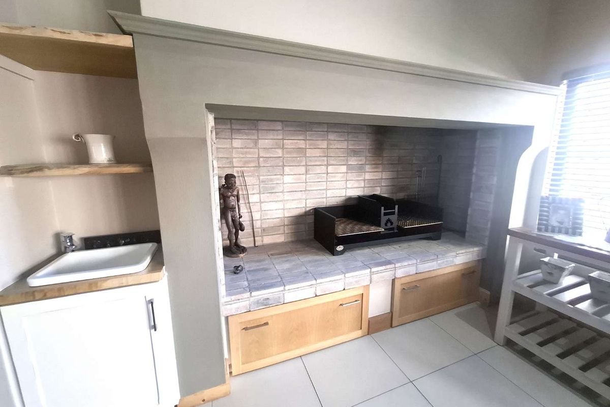 Indoor built-in braai area featuring a tiled hearth, integrated storage cabinetry, and a small prep sink with wooden shelving.