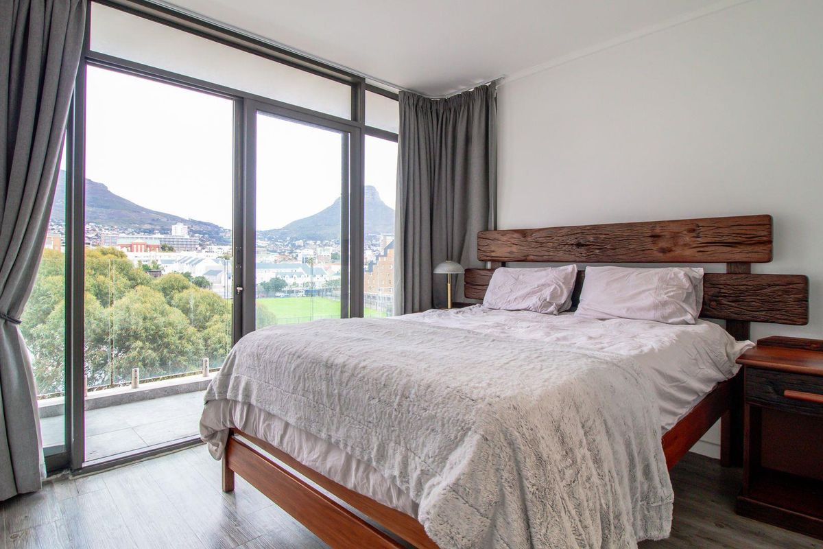 A bright bedroom featuring floor-to-ceiling sliding glass doors that open onto a balcony with scenic mountain and city views.