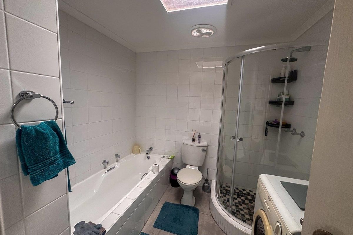 Functional bathroom featuring a built-in bathtub, separate curved glass shower enclosure, toilet, and integrated laundry space with tiled finishes.