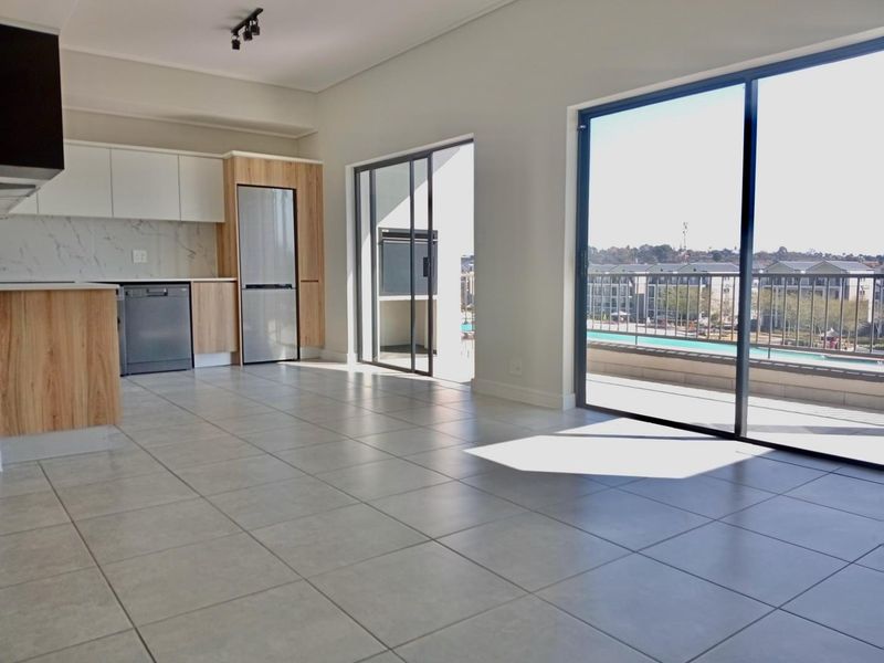 Modern open-plan kitchen and living area featuring tiled floors, sleek cabinetry, and large sliding doors opening onto a balcony with a built-in braai.