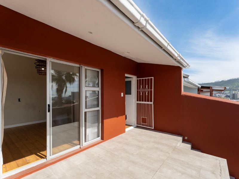 A spacious covered balcony featuring tiled flooring, sliding glass door access, and a security gate, offering an elevated outdoor area.