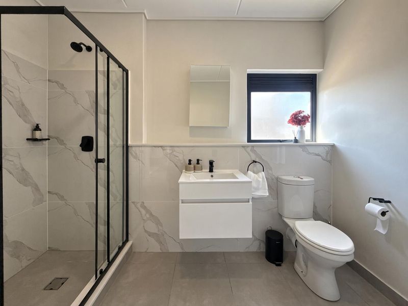 Modern bathroom featuring a walk-in shower with black-framed glass, a wall-mounted vanity, and elegant marble-look wall tiling.