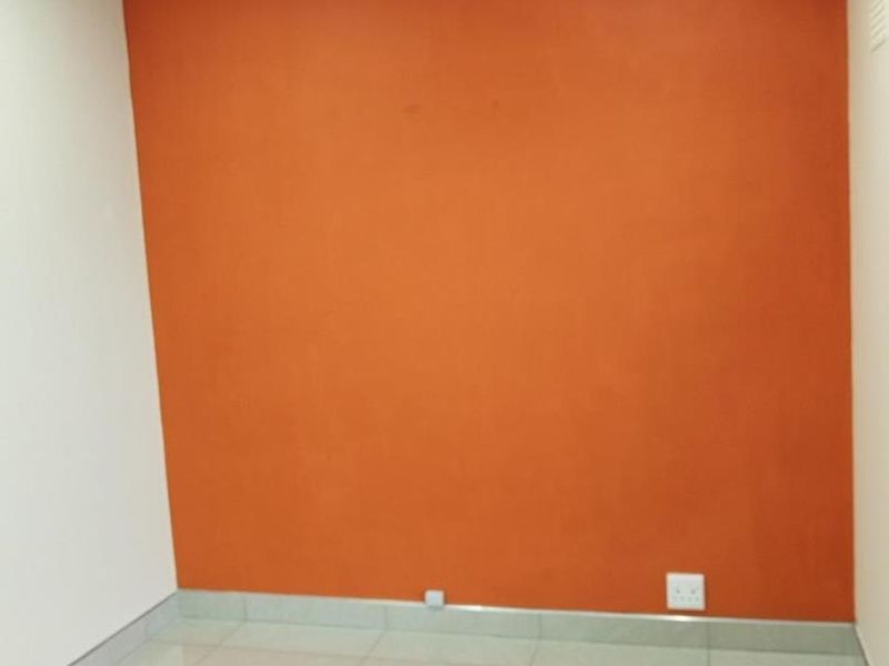A clean, empty office space featuring neutral tiled flooring, a vibrant orange accent wall, and a wall-mounted air conditioning unit.