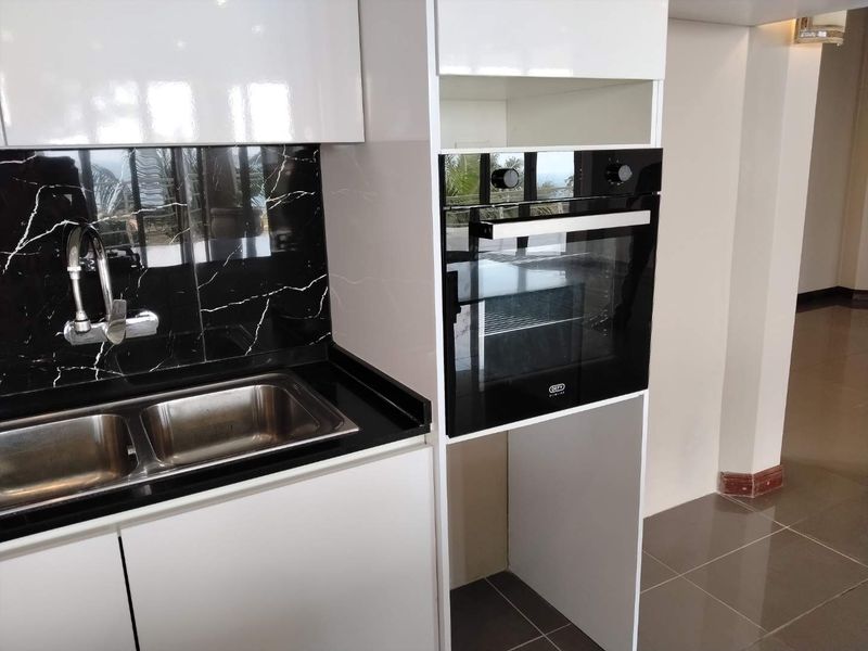 Modern kitchen featuring white cabinetry, a built-in oven, and a sleek black marble-look splashback with a double stainless steel sink.