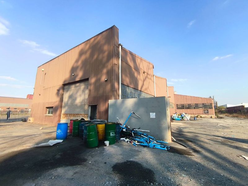 Rear view of an industrial warehouse facility featuring corrugated metal cladding, a large roller shutter door, and an expansive concrete yard area.