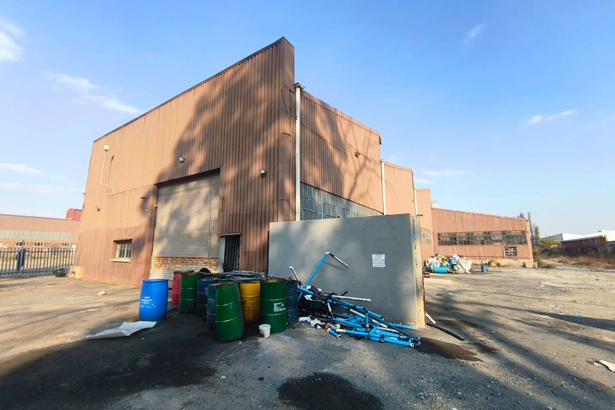 Rear view of an industrial warehouse facility featuring corrugated metal cladding, a large roller shutter door, and an expansive concrete yard area.