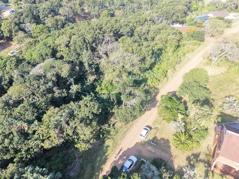 An aerial view of a vacant residential plot featuring dense natural vegetation and access via an unpaved road.