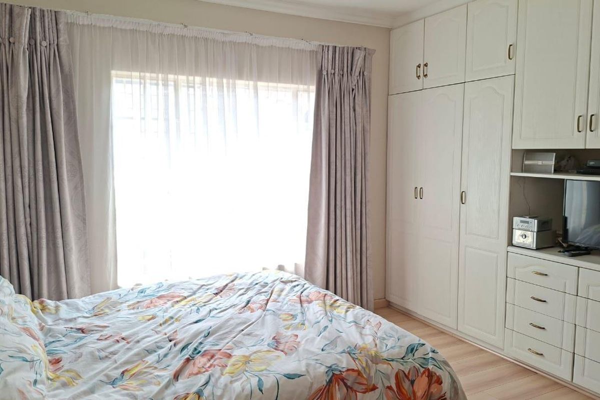 A bedroom featuring built-in white cabinetry with integrated storage and drawers, complemented by large windows with curtains.