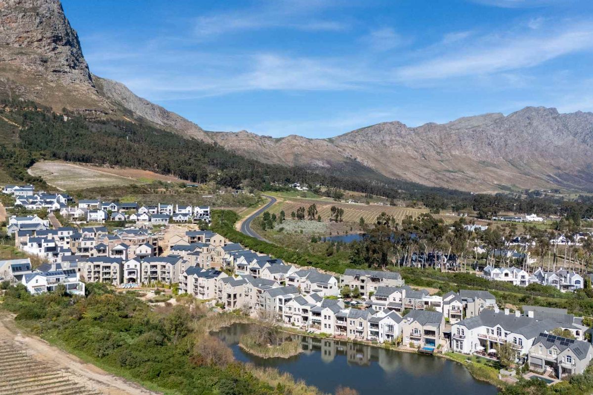 An aerial view of a residential estate nestled against a mountain range, featuring landscaped grounds and a central lake.