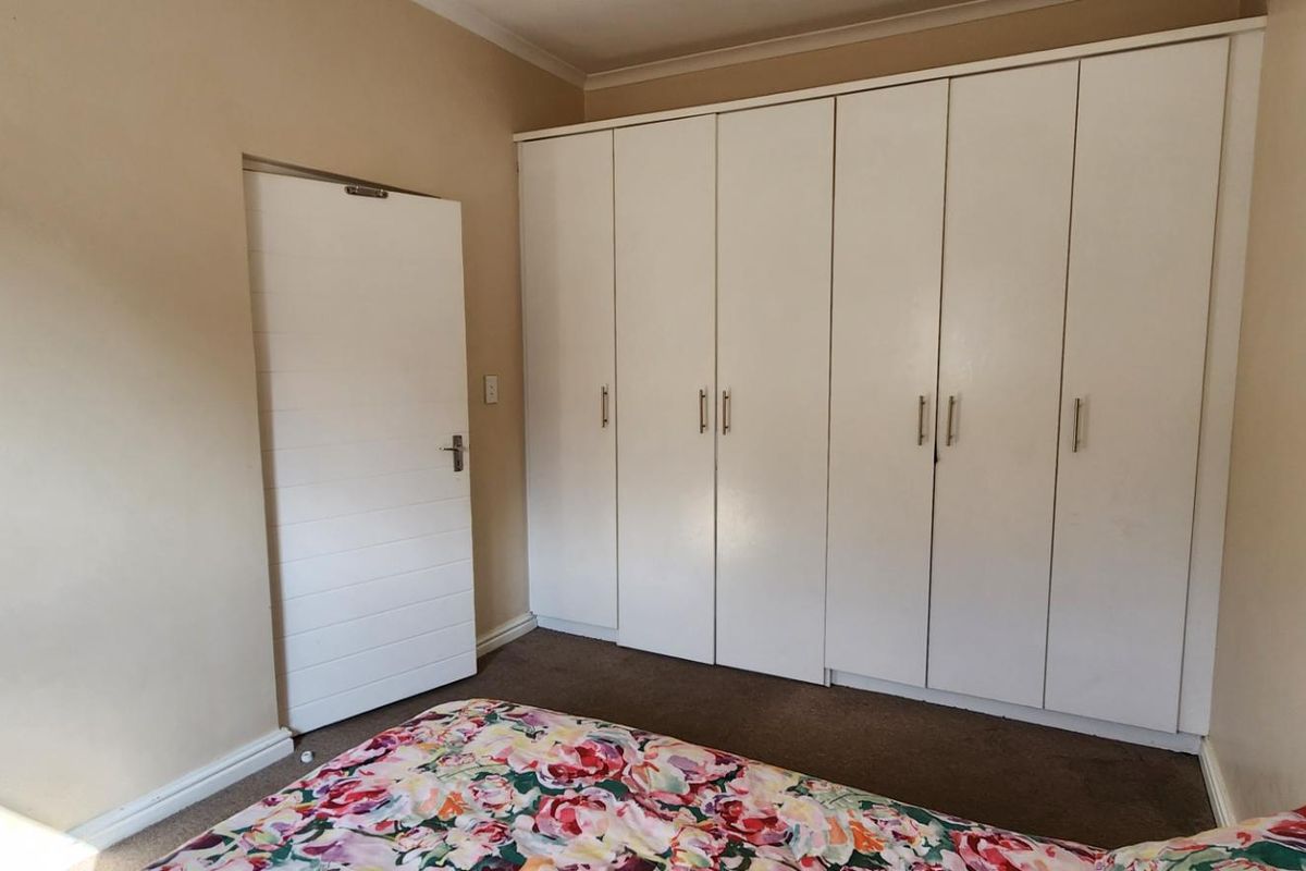 A bedroom featuring built-in cupboards with white doors, neutral wall paint, and carpeted flooring.