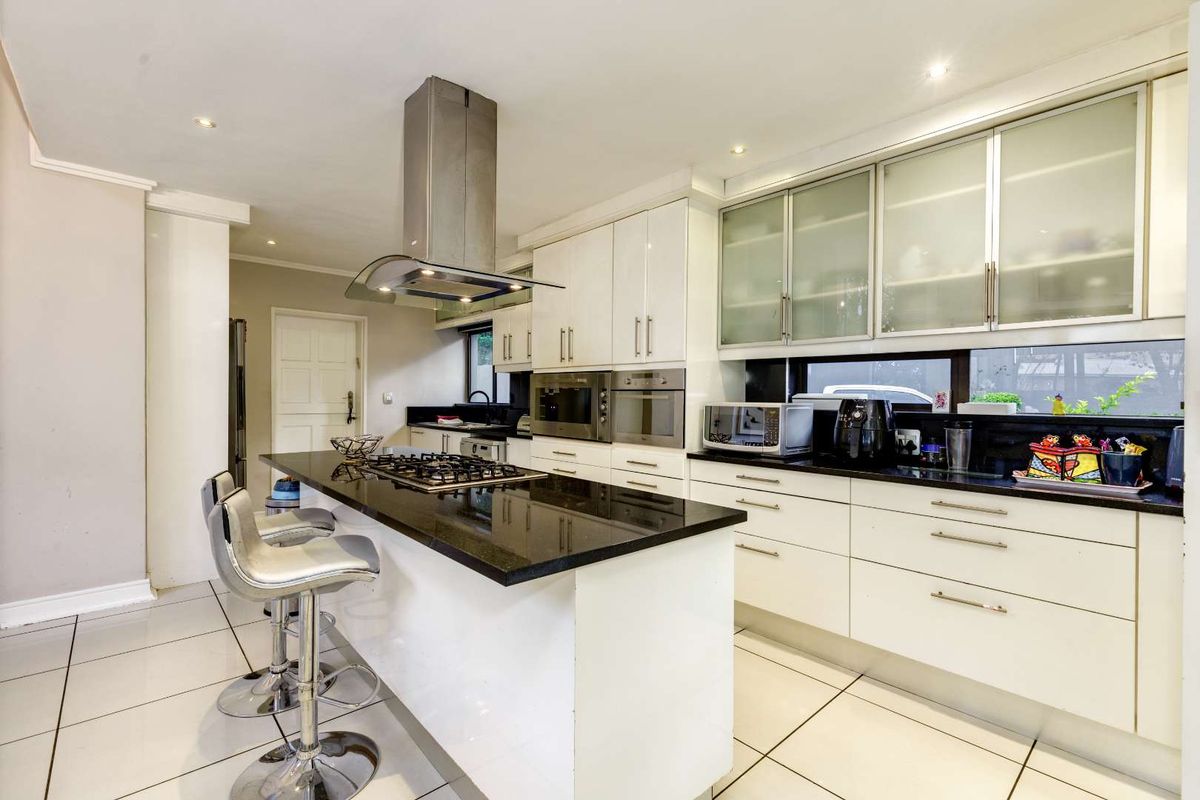 Modern kitchen featuring white cabinetry, black granite countertops, a central island with a gas hob, and built-in stainless steel appliances.