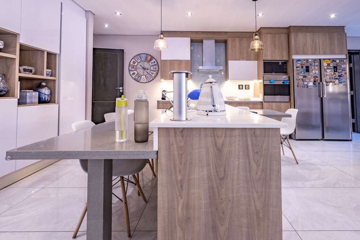 Modern kitchen featuring a large island with stone countertops, integrated appliances, sleek cabinetry, and contemporary pendant lighting.