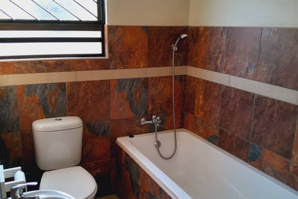 A functional bathroom featuring a bathtub with handheld shower, pedestal basin, toilet, and decorative slate-style wall tiling.