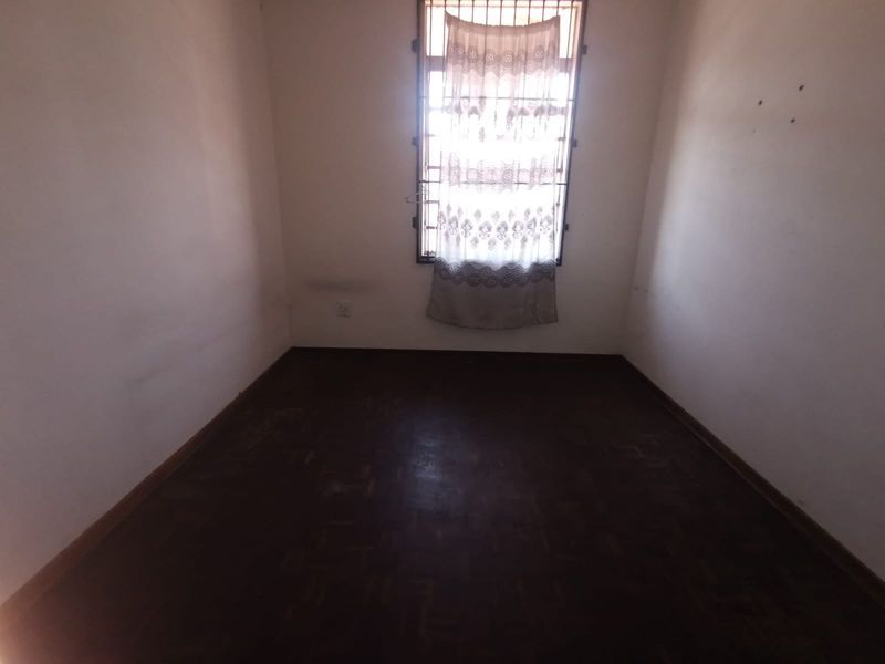 An empty bedroom featuring dark parquet flooring and a window fitted with security bars.