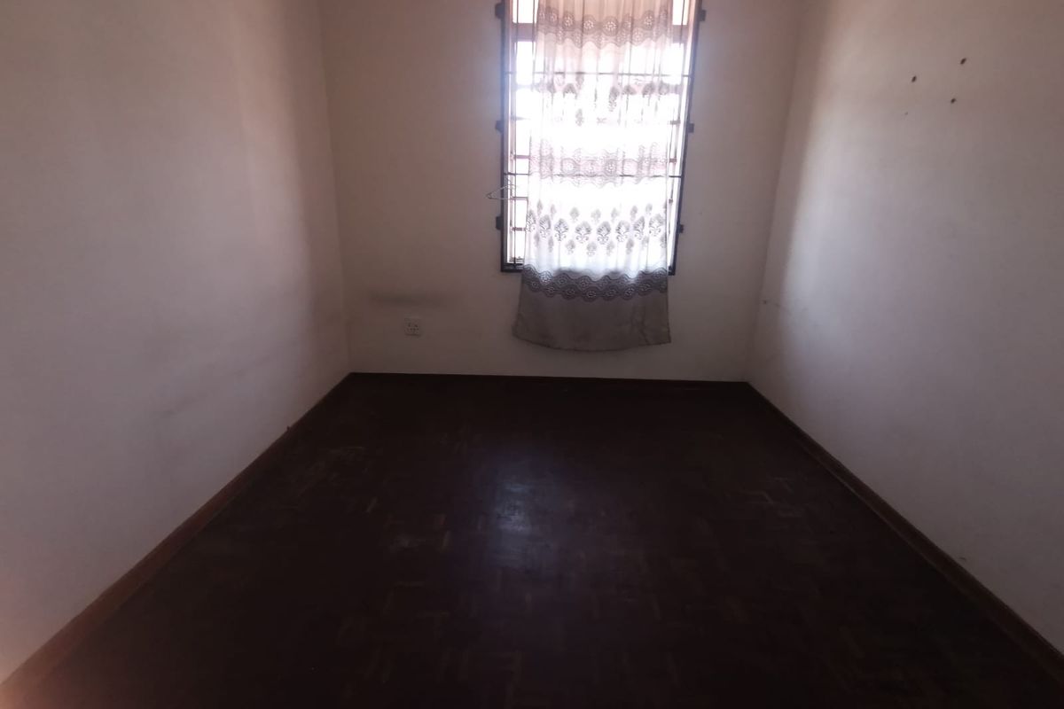 An empty bedroom featuring dark parquet flooring and a window fitted with security bars.