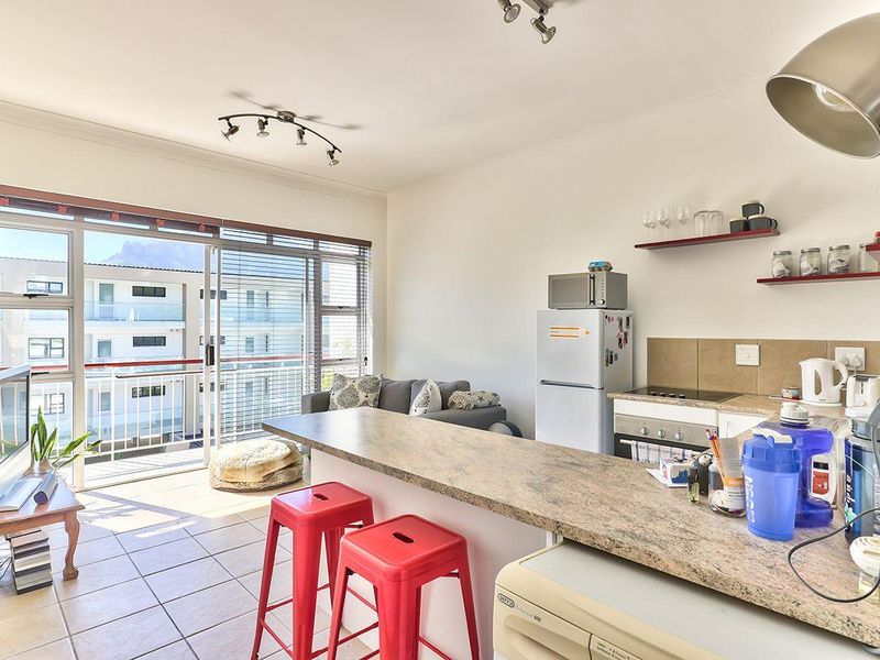 Open-plan living area featuring a kitchen with breakfast bar, tiled floors, and large sliding doors leading to a balcony with natural light.