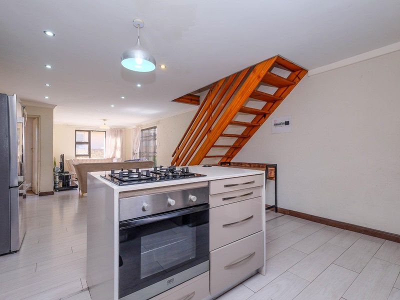 Open-plan living area featuring a modern kitchen island with gas hob and oven, complemented by a timber staircase and neutral tiled flooring.