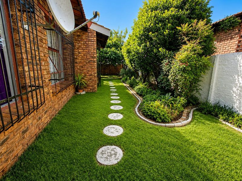 A well-maintained rear garden featuring a face brick exterior, a stone pathway, and established landscaping along the boundary wall.