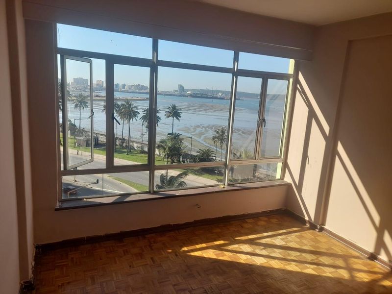 An empty living room featuring original parquet flooring and expansive windows offering panoramic coastal and city views.