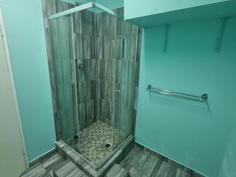 A functional bathroom featuring a raised shower enclosure with grey wood-look tiling and a chrome towel rail.