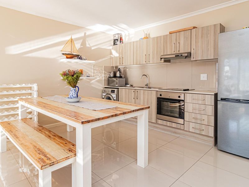 An open-plan kitchen and dining area featuring modern wood-look cabinetry, integrated appliances, tiled flooring, and a functional layout.