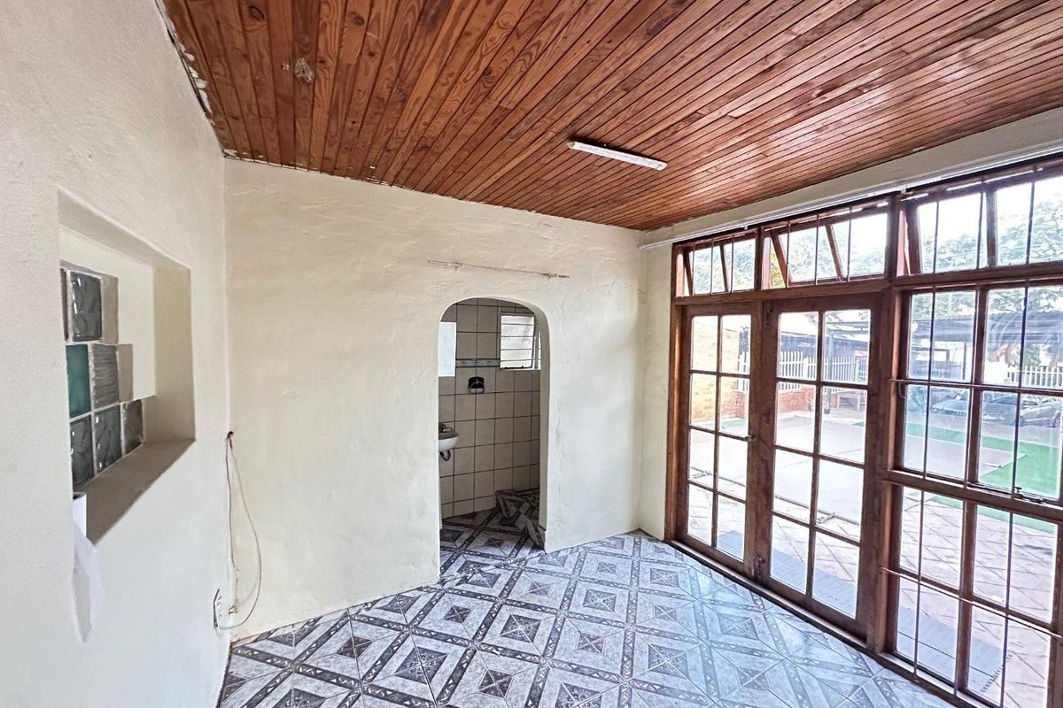 An empty room featuring a timber-clad ceiling, patterned floor tiles, and large wooden-framed glass doors leading to an outdoor area.