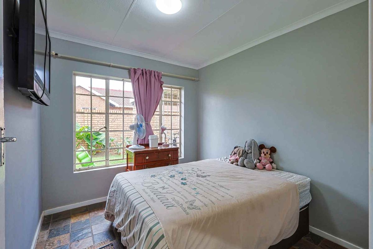 A bedroom featuring slate tile flooring, a large window with security bars, and neutral wall paint.