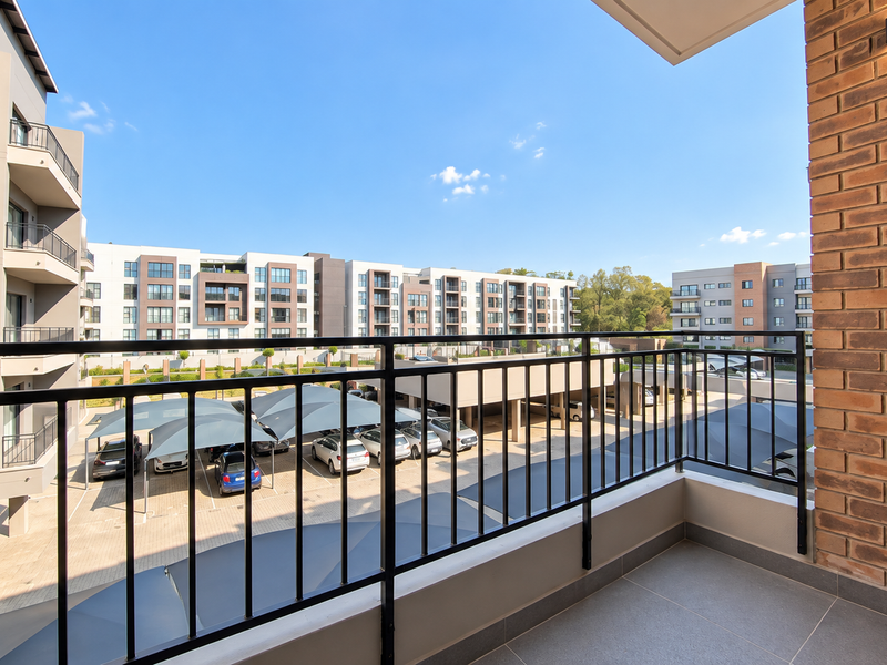 A modern, well-maintained balcony featuring tiled flooring, a metal balustrade, and an exposed brick feature wall, overlooking the apartment complex parking area.