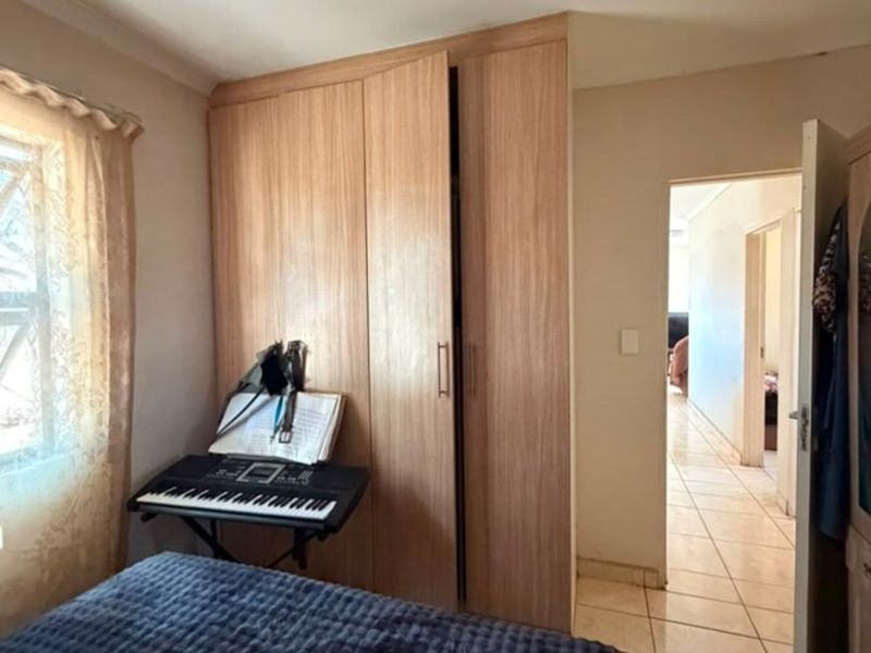 A bedroom featuring built-in wooden wardrobes and tiled flooring, with a doorway leading to an adjacent hallway.