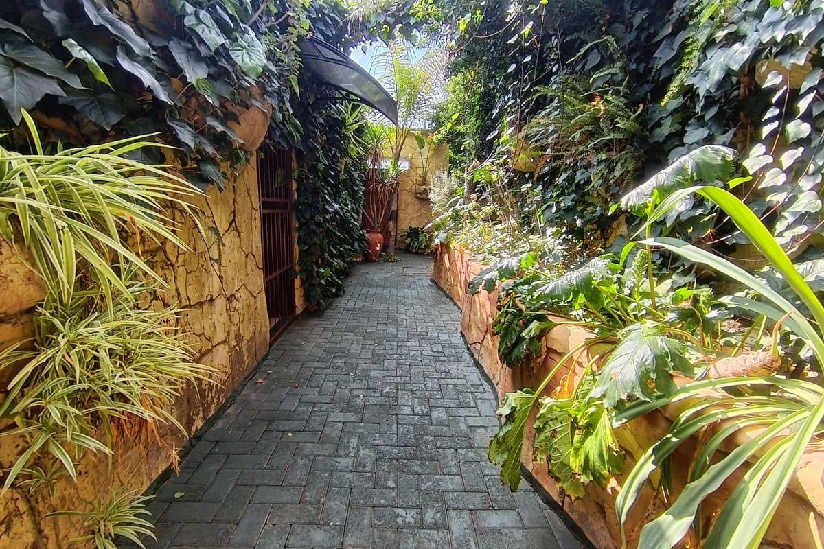 A landscaped garden pathway featuring stone-clad walls, lush climbing ivy, and durable paver flooring leading to a secure entrance.