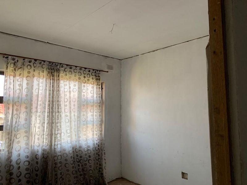 An empty bedroom featuring a ventilation brick and basic window treatment, requiring cosmetic updates to the ceiling and wall finishes.