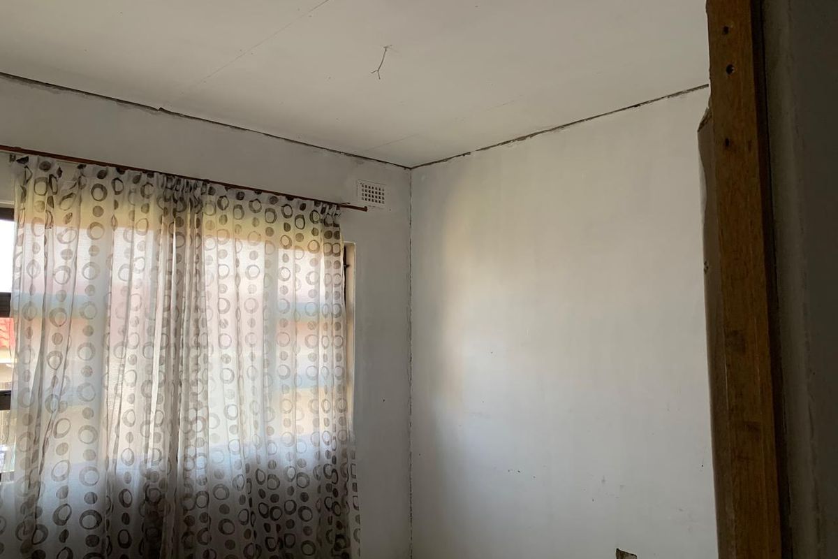 An empty bedroom featuring a ventilation brick and basic window treatment, requiring cosmetic updates to the ceiling and wall finishes.