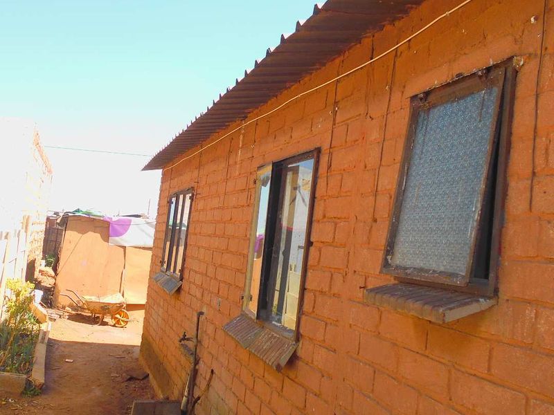 Exterior view of a simple brick structure featuring metal roofing and casement windows, situated in a basic outdoor setting.