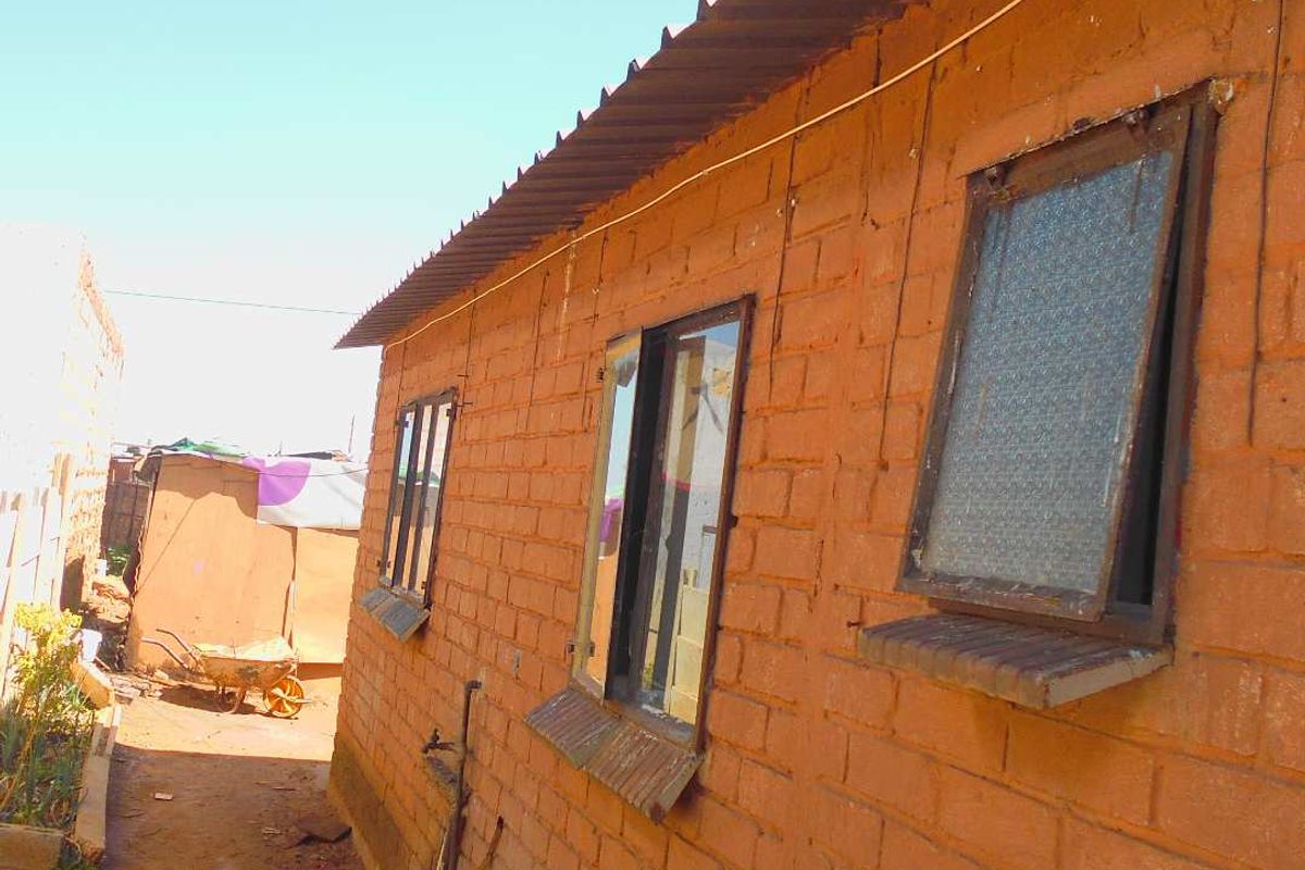Exterior view of a simple brick structure featuring metal roofing and casement windows, situated in a basic outdoor setting.