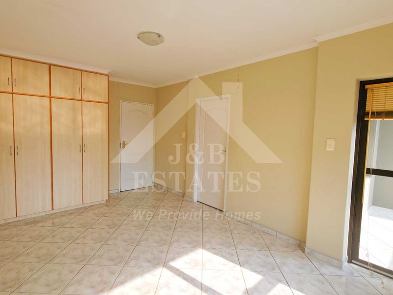 An empty bedroom featuring built-in cupboards, tiled flooring, and a sliding door leading to an outdoor area.