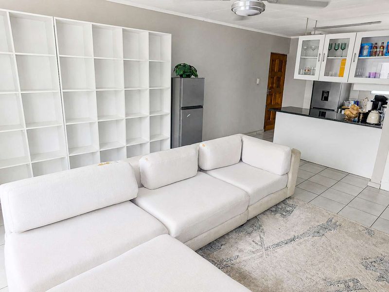 Open plan living area featuring tiled flooring, a ceiling fan, and a kitchen with granite countertops and white cabinetry.