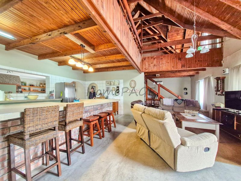 Spacious open-plan living area featuring exposed timber ceilings, trusses, a brick breakfast bar, and a mezzanine level with a timber staircase.