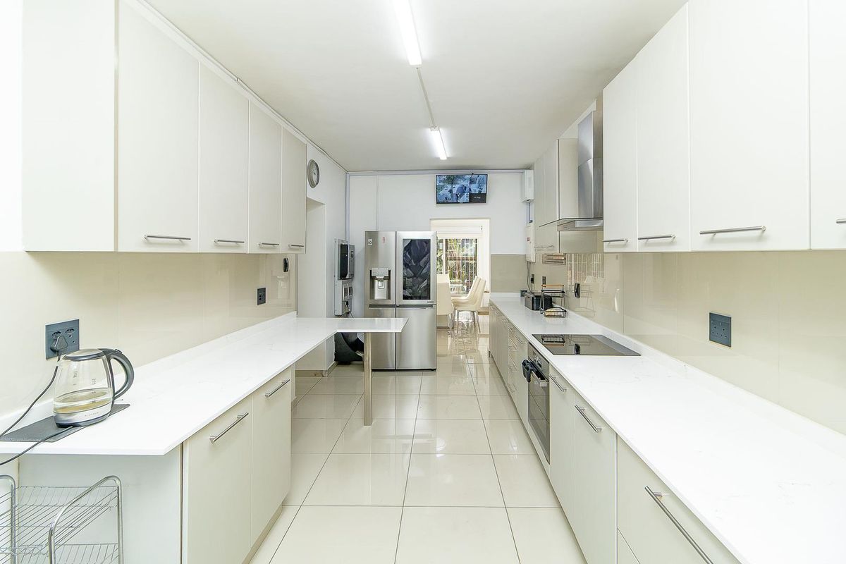 Modern galley-style kitchen featuring sleek white cabinetry, quartz countertops, integrated appliances, and polished tiled flooring, offering a clean and functional workspace.
