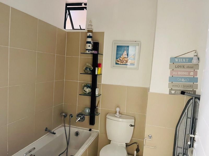 A functional bathroom featuring a built-in bathtub with shower mixer, a standard toilet, and neutral wall tiling.