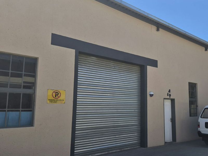 Industrial unit exterior featuring a large roller shutter door, pedestrian access, and steel-framed windows with paved frontage.