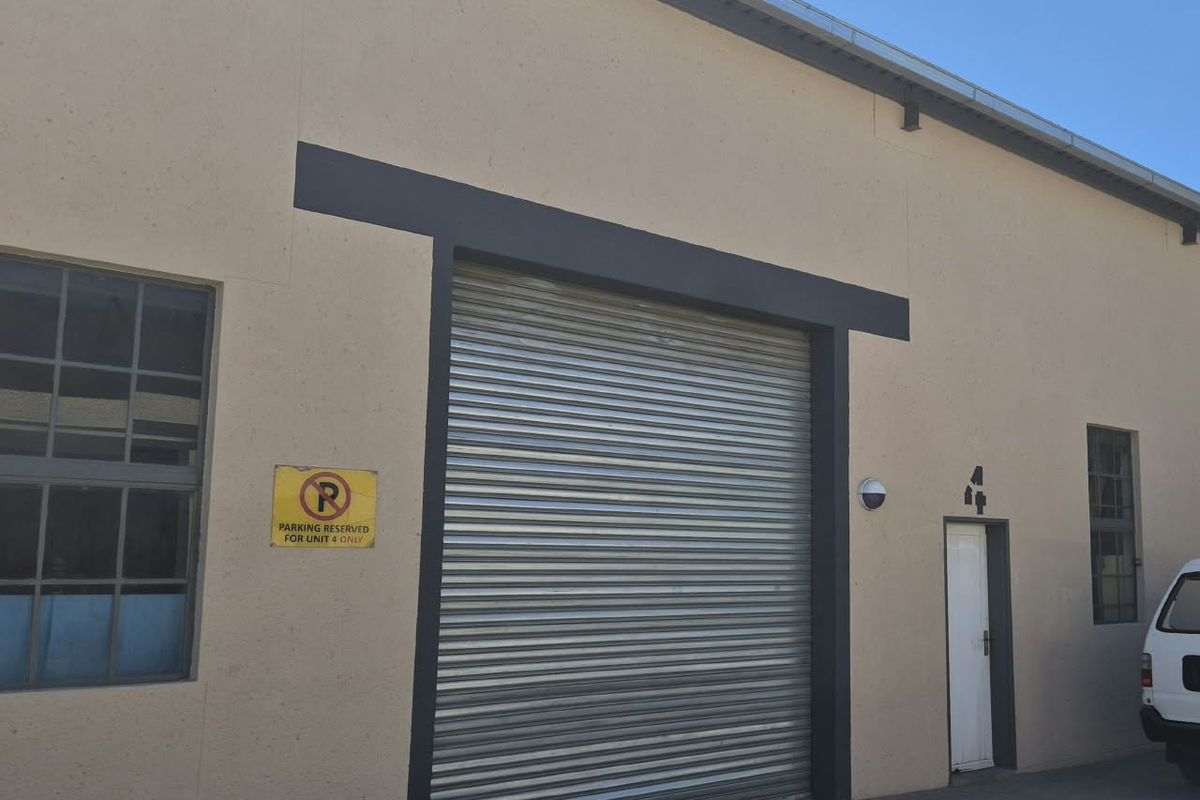 Industrial unit exterior featuring a large roller shutter door, pedestrian access, and steel-framed windows with paved frontage.