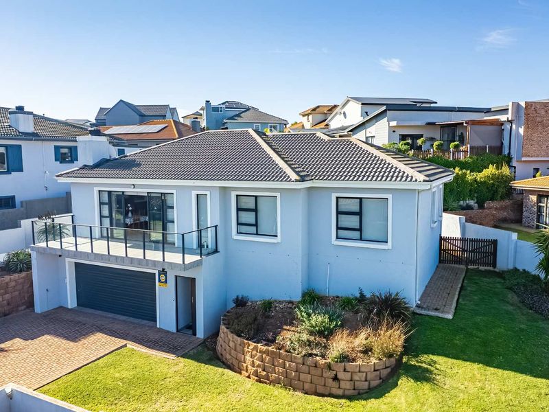 Aerial view of a modern residential property featuring a tiled roof, a balcony with glass balustrades, an automated garage, and a landscaped garden.