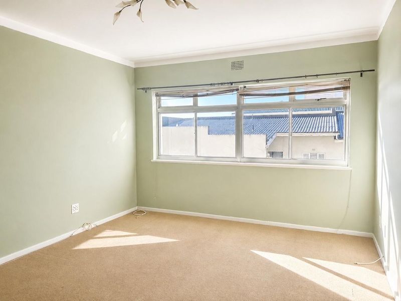 A bright, empty bedroom featuring neutral carpet flooring, soft green walls, and a large sliding window with a curtain rod.
