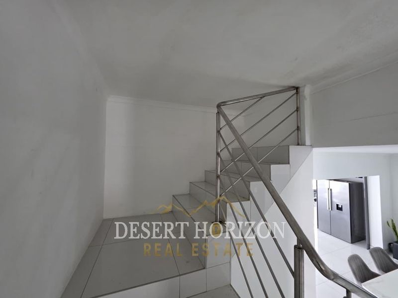 A clean, minimalist staircase featuring tiled steps and a modern stainless steel balustrade, providing a bright and open transition between levels.