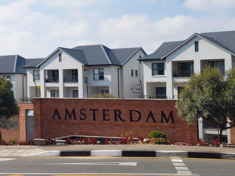 Street view of the Amsterdam apartment complex featuring modern multi-story residential buildings with balconies and a prominent brick entrance wall.